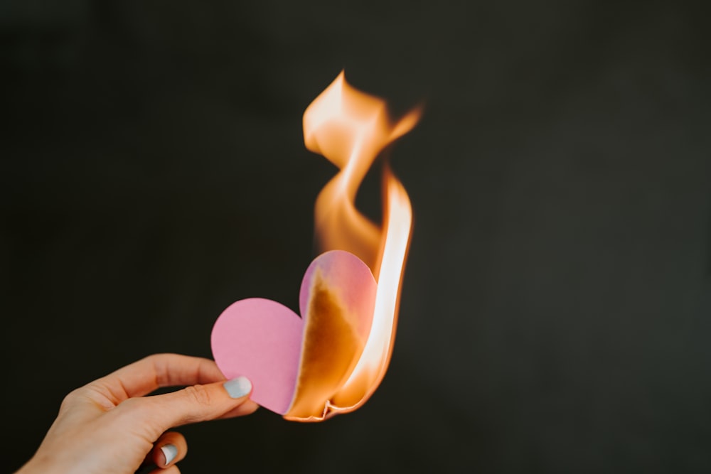 a person holding a paper heart in front of a fire