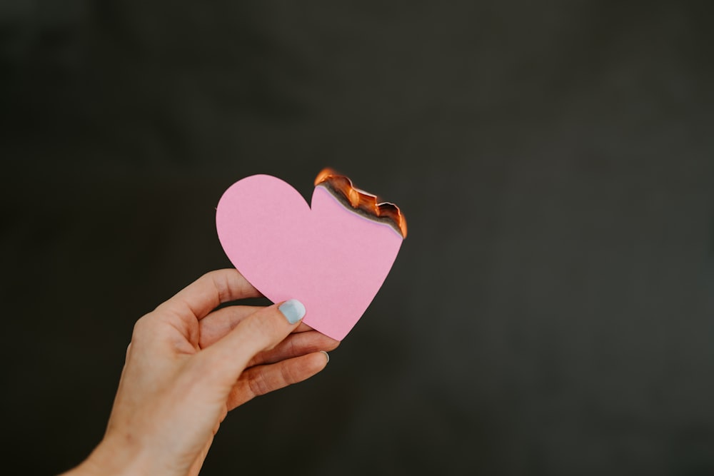 a person holding a pink heart shaped piece of paper