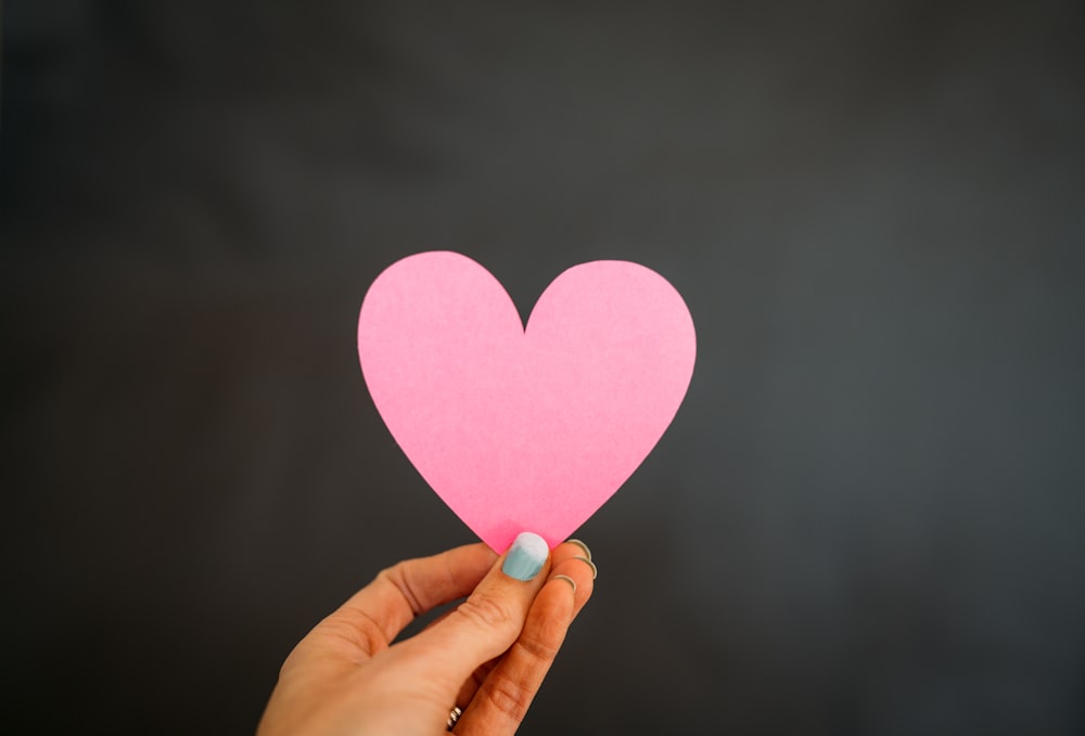 a person holding a pink paper heart in their hand
