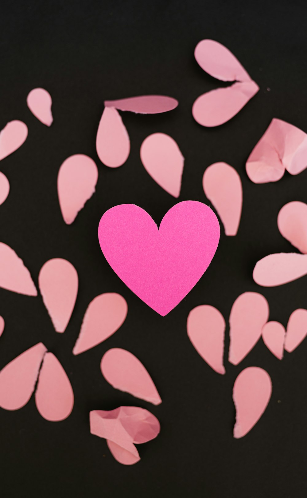 a pink heart surrounded by pink petals on a black background