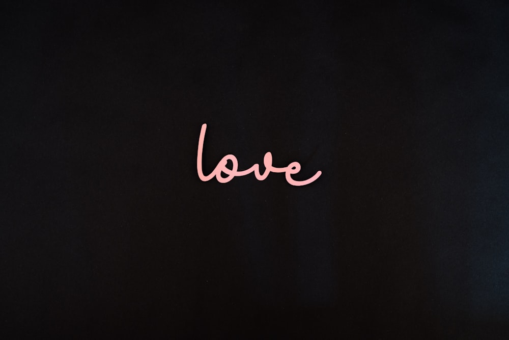 the word love is written in pink on a black background