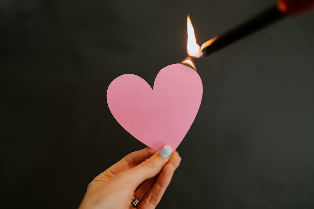 a person holding a paper heart with a lighter in the background