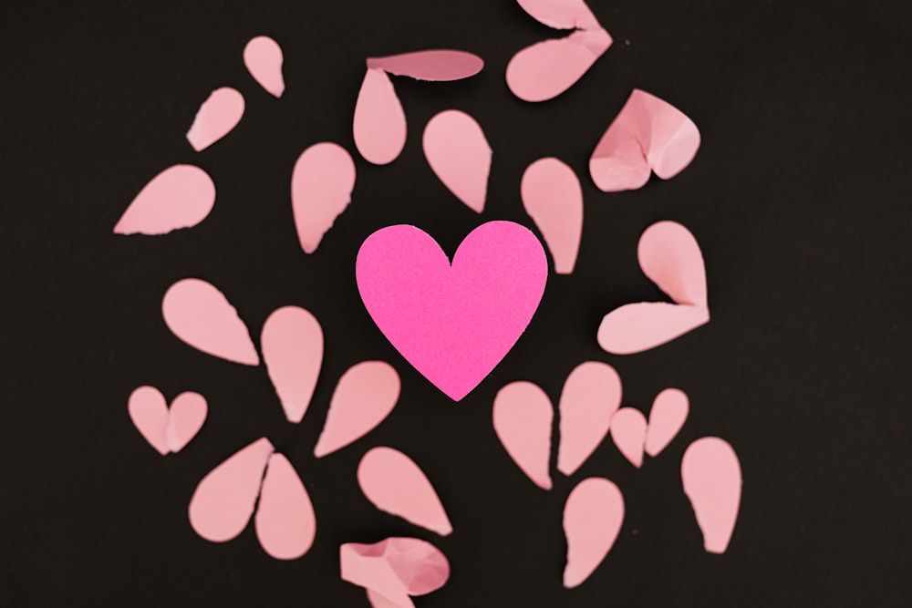 un cœur rose entouré de confettis roses sur fond noir