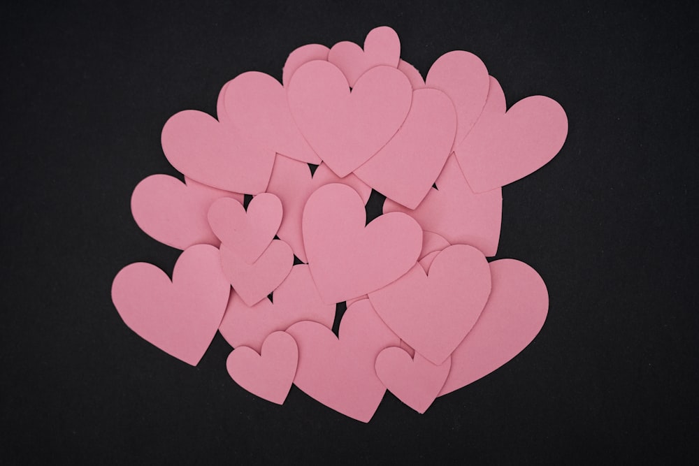 a pile of pink paper hearts on a black background