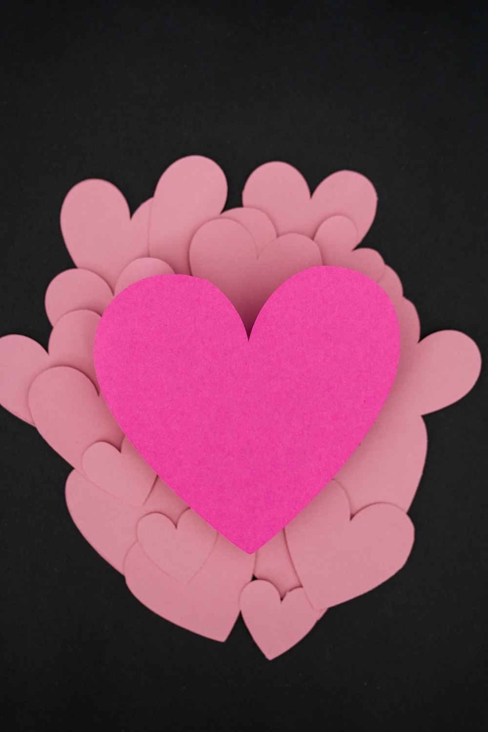 Ein rosa Herz umgeben von rosa Herzen auf schwarzem Hintergrund