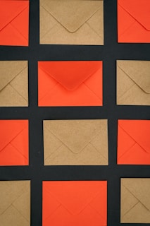 A grid of envelopes placed on a dark background, alternating between red and brown colors. The envelopes are evenly spaced, creating a pattern with distinct contrasts between the vibrant red and the subdued brown tones.