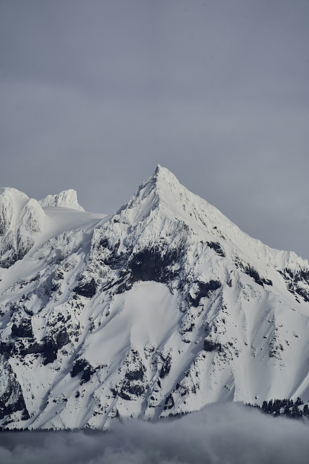 a mountain covered in snow and clouds under a gray sky