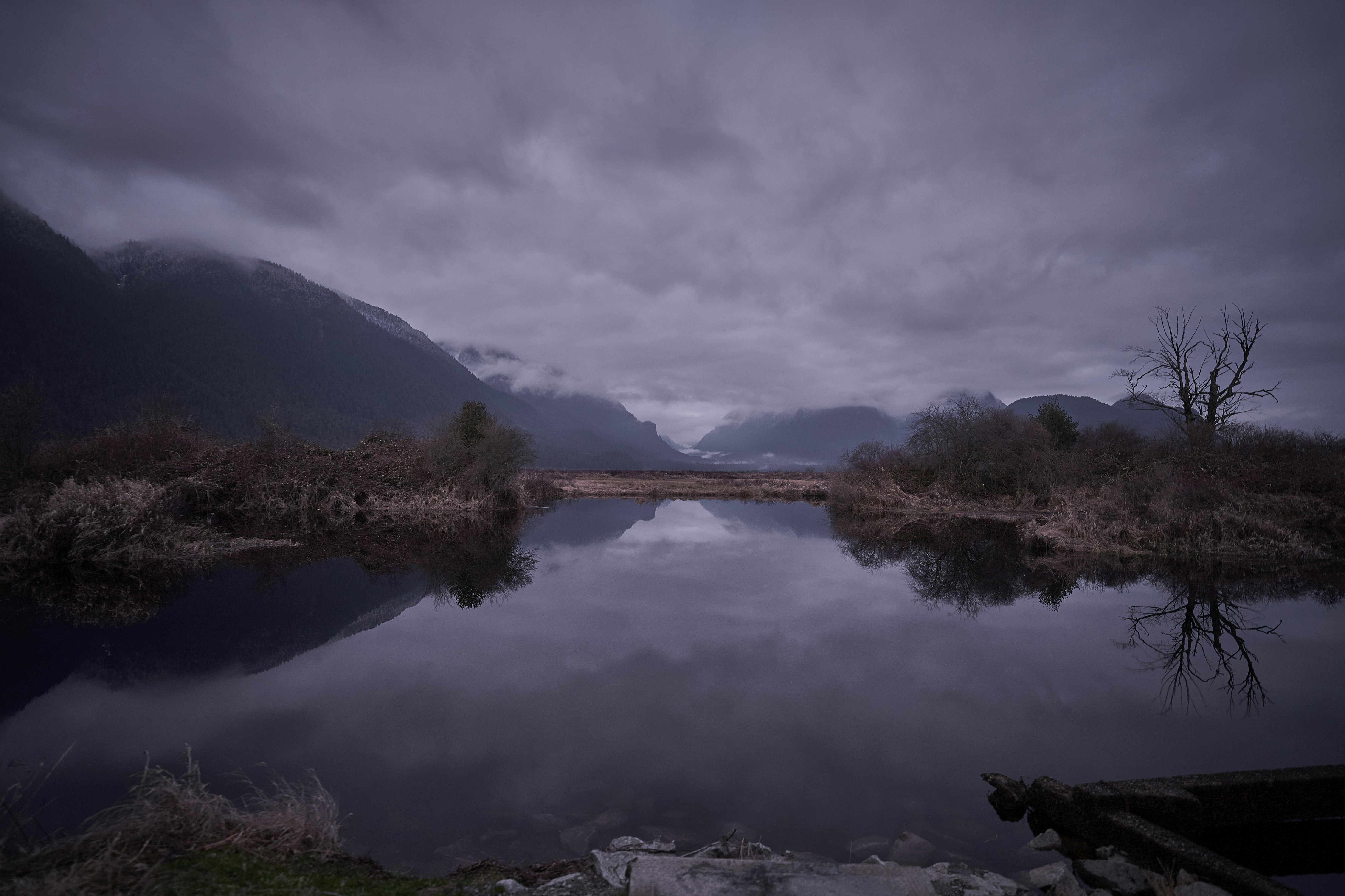 a body of water surrounded by mountains under a cloudy sky