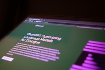 A computer screen displaying a webpage about ChatGPT, focusing on optimizing language models for dialogue. The webpage has text describing the model and includes the OpenAI logo. The background is green with some purple graphical elements on the side.