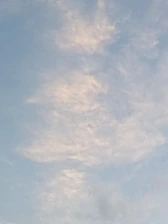 A peaceful sky with light blue hues and wisps of soft white clouds drifting gently.