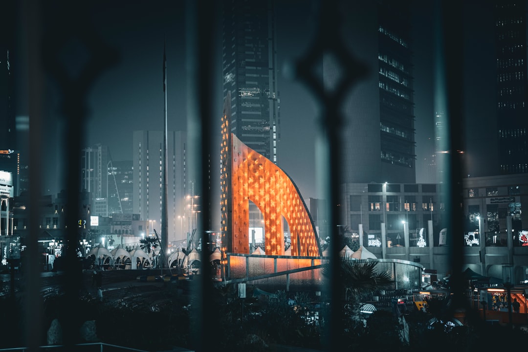 a view of a building through a fence at night, City square