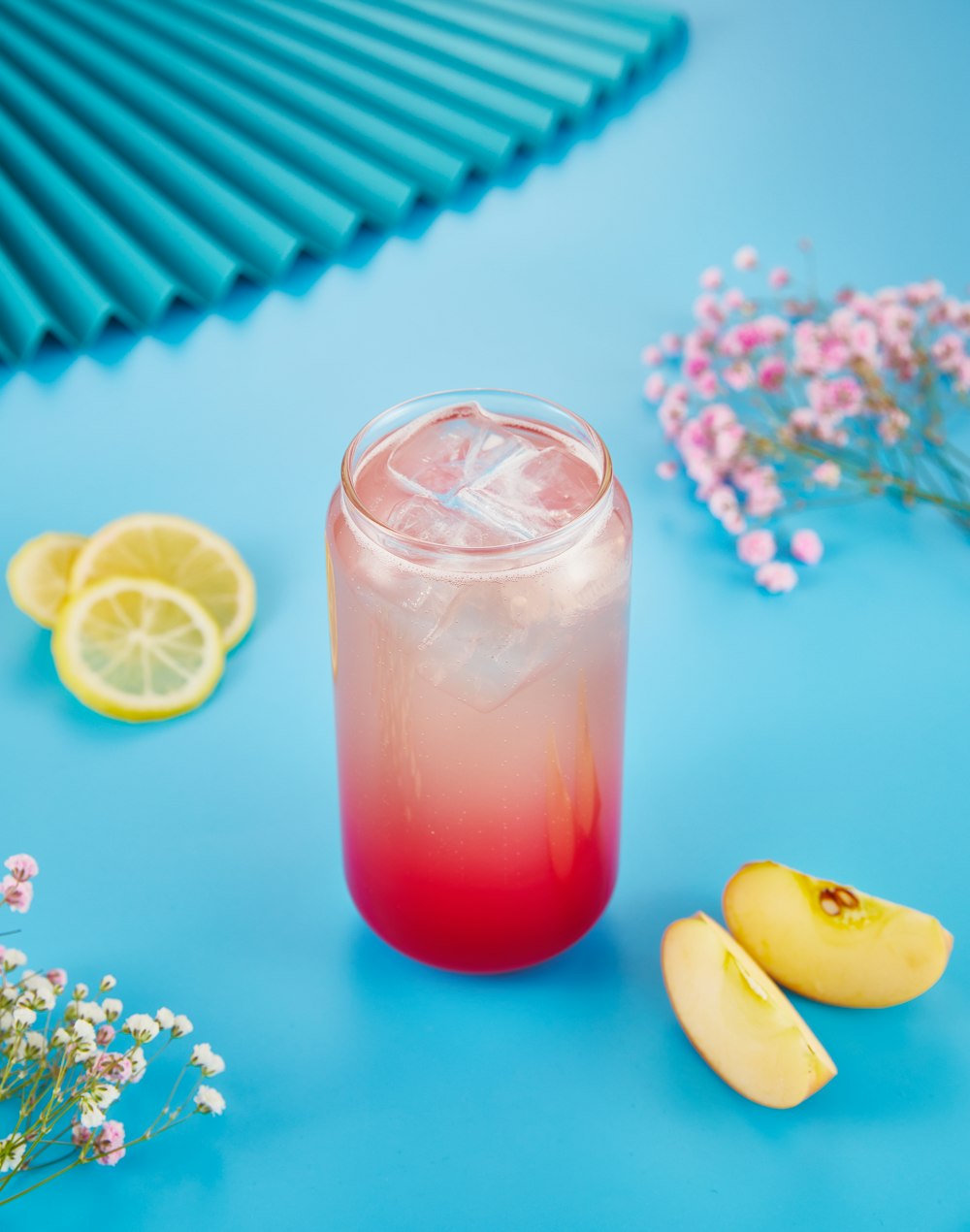 un vaso de limonada junto a limones y flores en rodajas