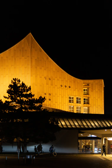 A sleek modern building with sharp angles and concrete gray facade, accented by warm golden lighting at dusk.
