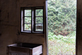 Rustic wooden window with glass panes opening to a sunlit garden.