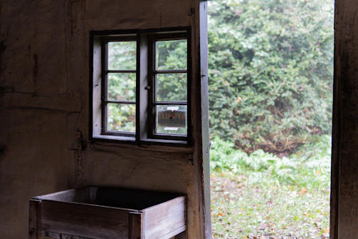 Rustic wooden window with glass panes opening to a sunlit garden.