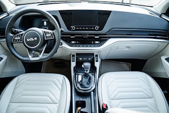 Modern car interior featuring a sleek dashboard design with a digital display, a multi-functional steering wheel, and an automatic gear shift. The interior is designed with light-colored leather seats and a clean, minimalist aesthetic.