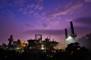 A panoramic view of a large industrial power plant at dusk, with glowing lights and towering structures.