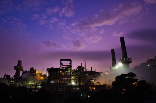 A large industrial gas generator set against a backdrop of a sprawling power plant at dusk.