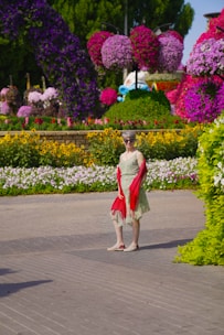 A woman in a flowing dress and delicate scarf, walking through a blooming garden on a bright day.