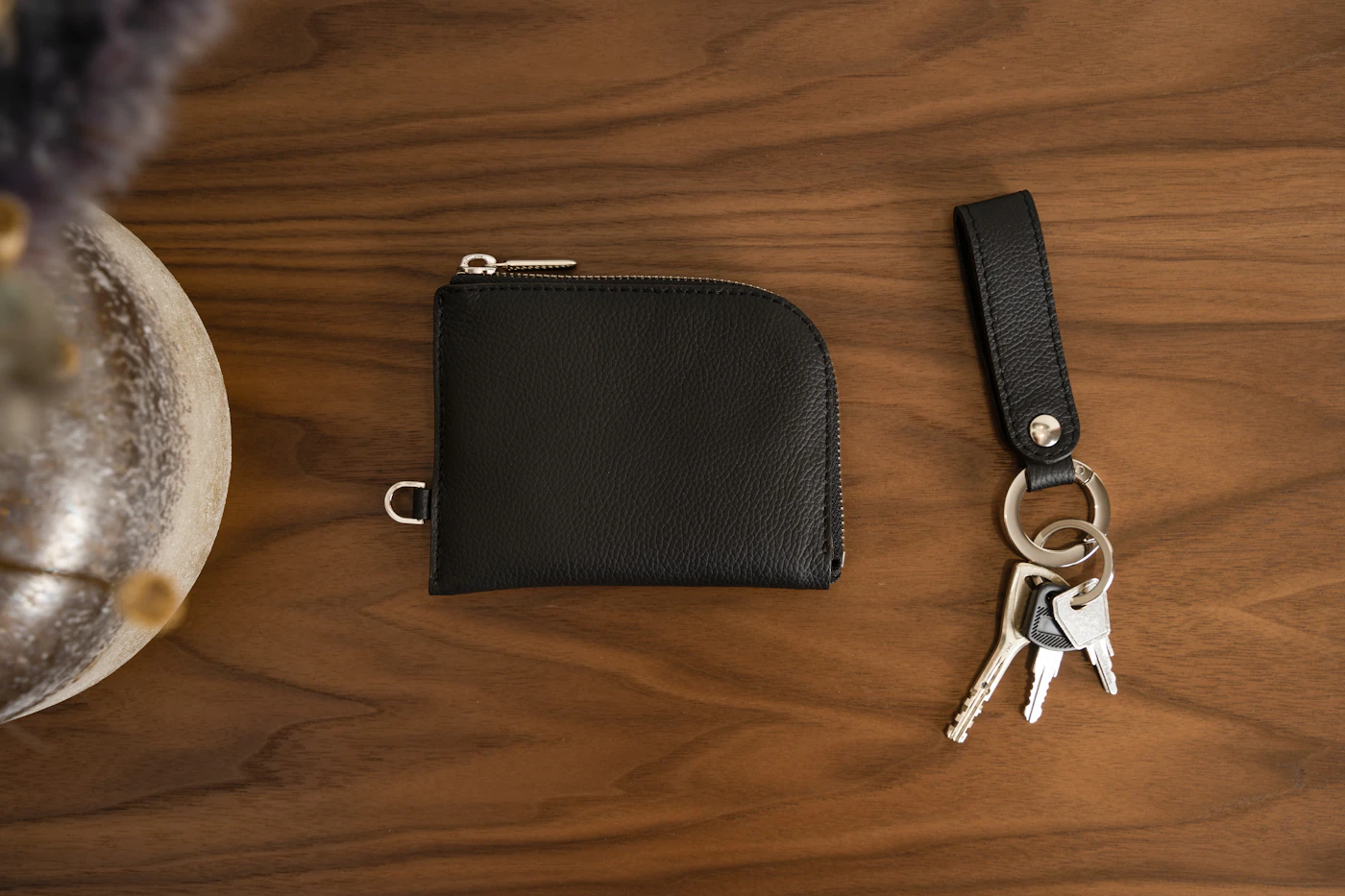 A black zip wallet and a set of keys lying on a walnut table