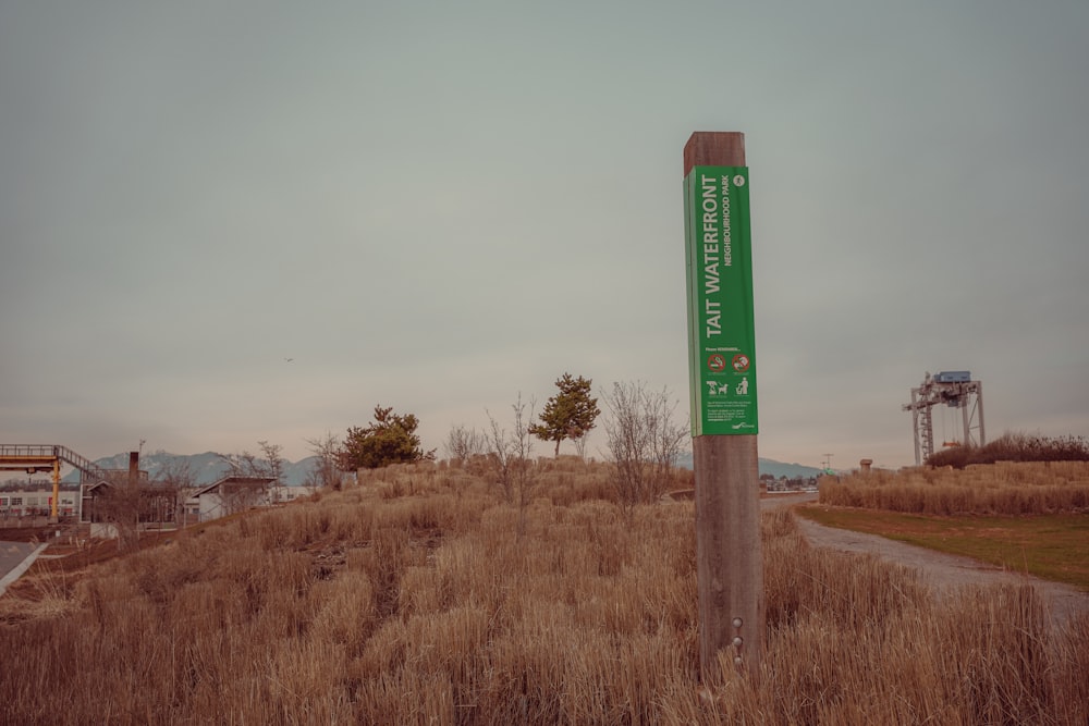 a green sign sitting on top of a dry grass covered field