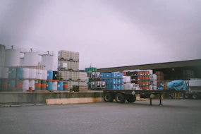 A detailed shot of raw commodities like grains and oil barrels stacked in a warehouse.