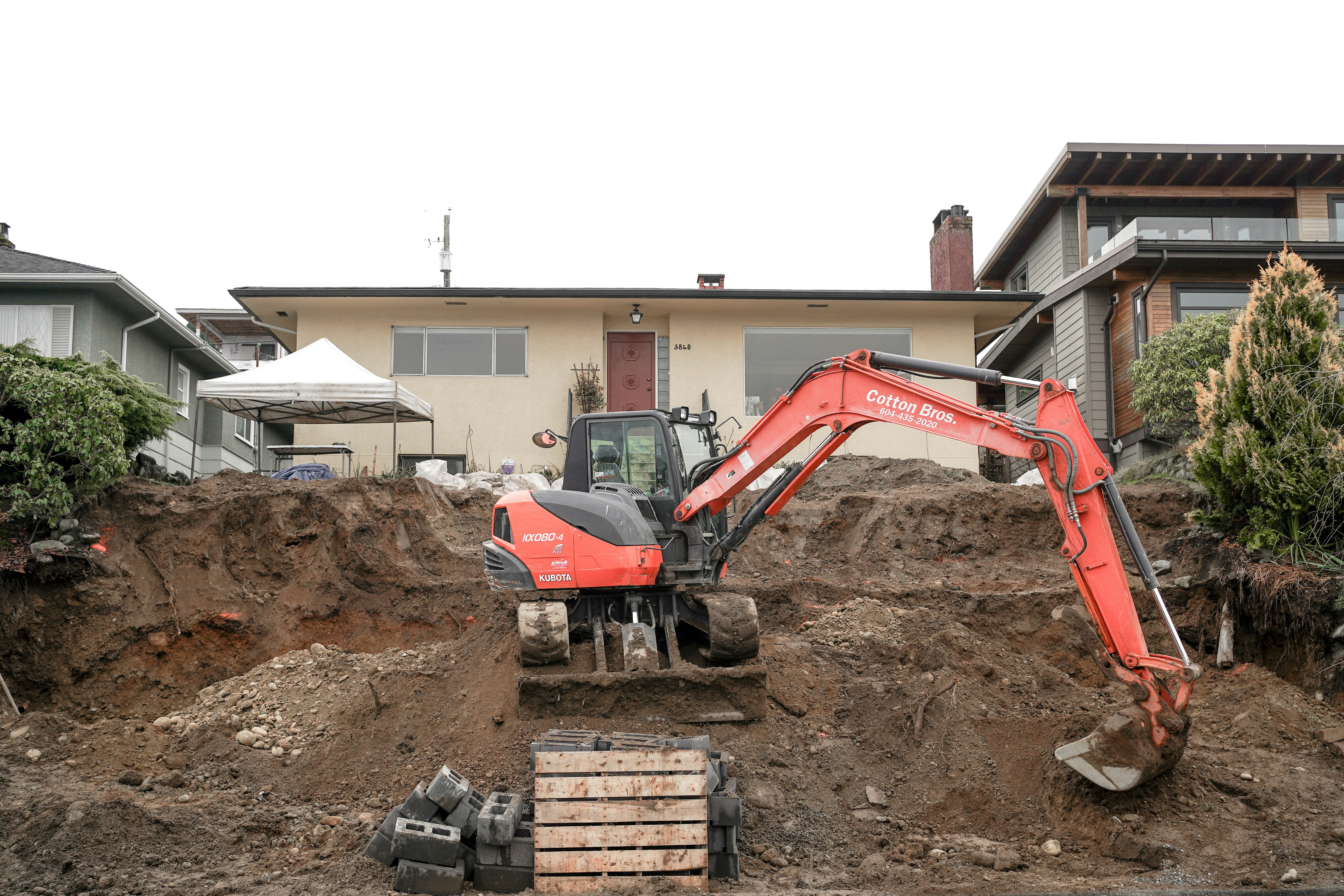 An excavator digging a trench alongside a home's foundation - Exterior basement wall waterproofing