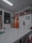 A room with a white ceiling and fluorescent lighting, featuring a large central table and several office doors with glass panels. There are red chairs around the table, framed certificates and art on the walls, and a fire extinguisher mounted on the wall.