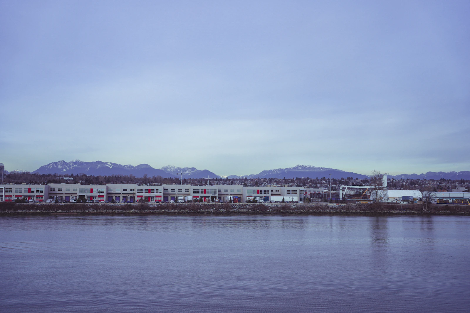 Waterfront condo buildings across a calm river with snow capped coastal mountains rising behind them