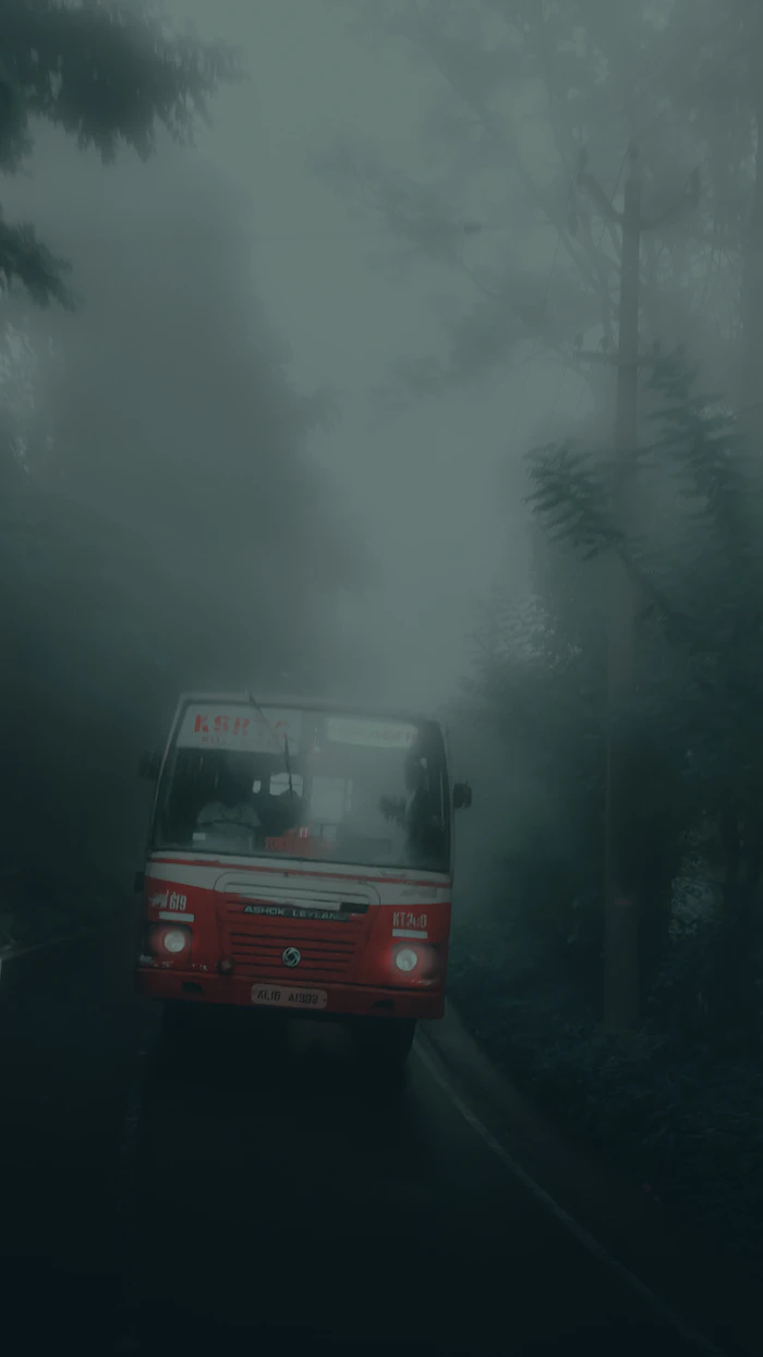 A red Kerala state bus on a misty hill road