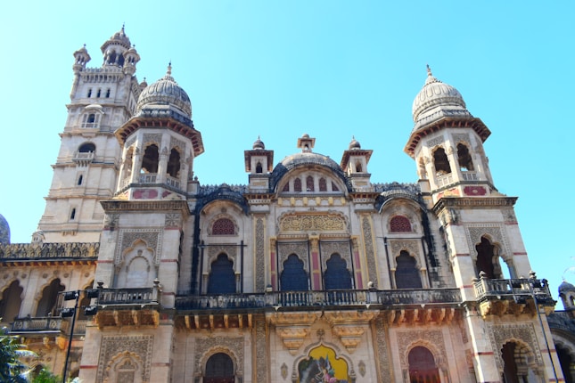 An intricately designed, ornate building with large domes and detailed carvings is seen. The structure features tall spires and decorative arches, showcasing elaborate architectural craftsmanship.
