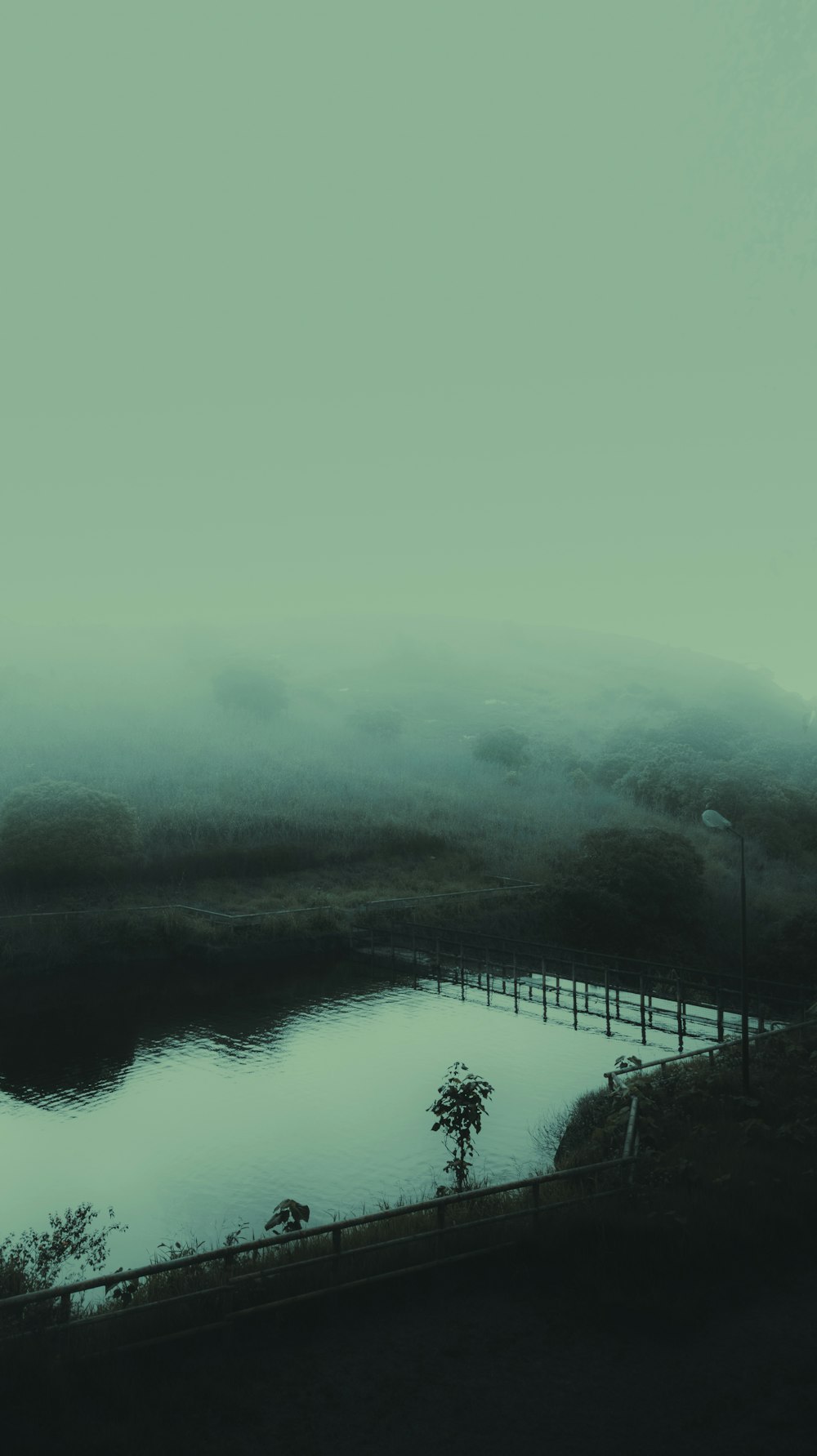a foggy landscape with a lake and a fence