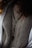 A close-up view of a person wearing a textured knit sweater with a rosary featuring wooden beads and a cross pendant draped over it. The outerwear appears to have a wool or fur-lined interior.