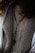 A close-up view of a person wearing a textured knit sweater with a rosary featuring wooden beads and a cross pendant draped over it. The outerwear appears to have a wool or fur-lined interior.