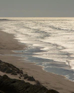 Quiet, empty beach under soft overcast skies with gentle waves.