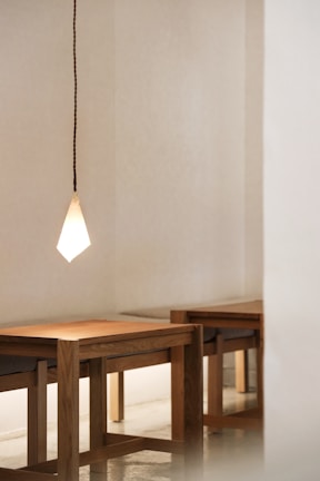 A sleek mid-century pendant light casting a warm glow over a minimalist wooden dining table.