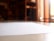 A close-up view of a blank white paper on a reflective surface, with a blurred background that includes shelves and warm lighting.