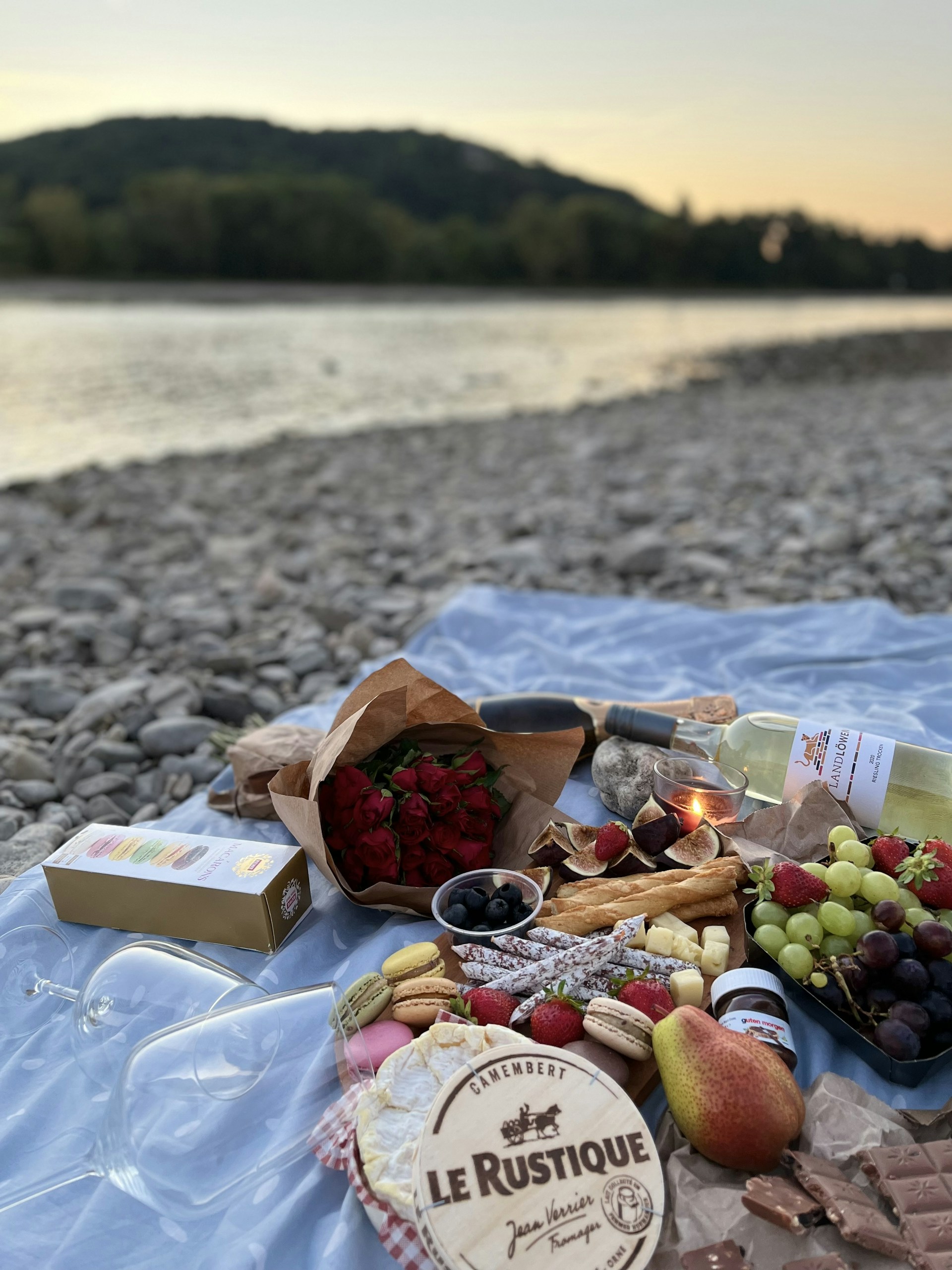 A cozy picnic setup with homemade food on a wooden table overlooking lush green valleys and distant mountains at sunset.