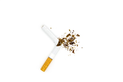 A cigarette is broken in half, with tobacco scattered around it on a plain white background.