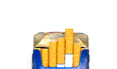 An open cigarette pack reveals several cigarettes, neatly lined up with their filter tips visible. The pack is predominantly blue with a metallic interior flap.