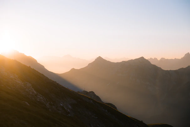 A serene mountain landscape at sunrise with soft golden light illuminating the peaks.