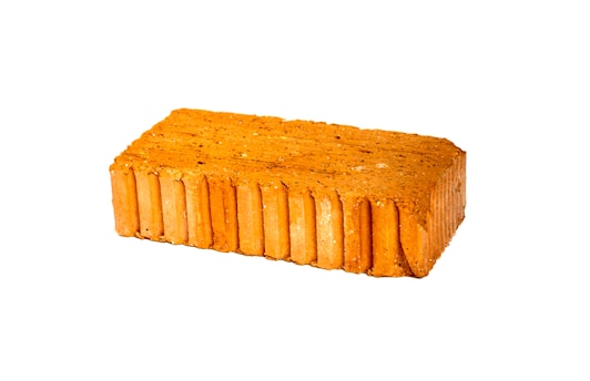 A rectangular red brick with a textured surface and visible sedimentary layers is displayed against a white background.