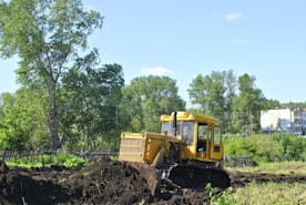 a bulldozer digging through a field with trees in the background