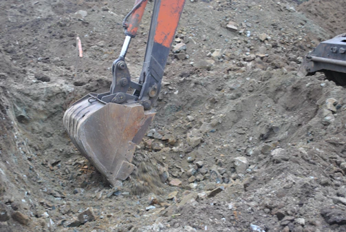 Close-up of a durable excavator bucket digging earth on a construction site.