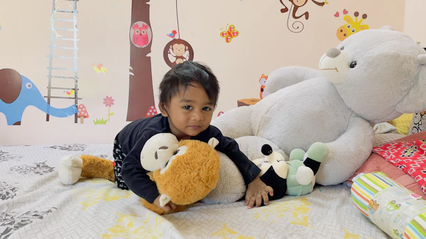 A smiling toddler playing with a plush animal toy in a cozy playroom.