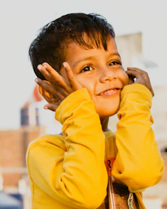 a young boy holding his hands up to his face