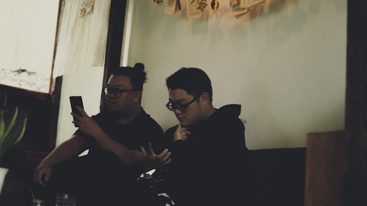 A cozy, dimly lit room with two people sharing a playful and intimate moment over a chat interface on their phones.
