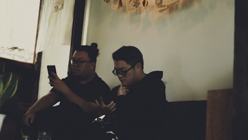 Two people exchanging messages on their phones, their screens glowing warmly in a cozy setting.