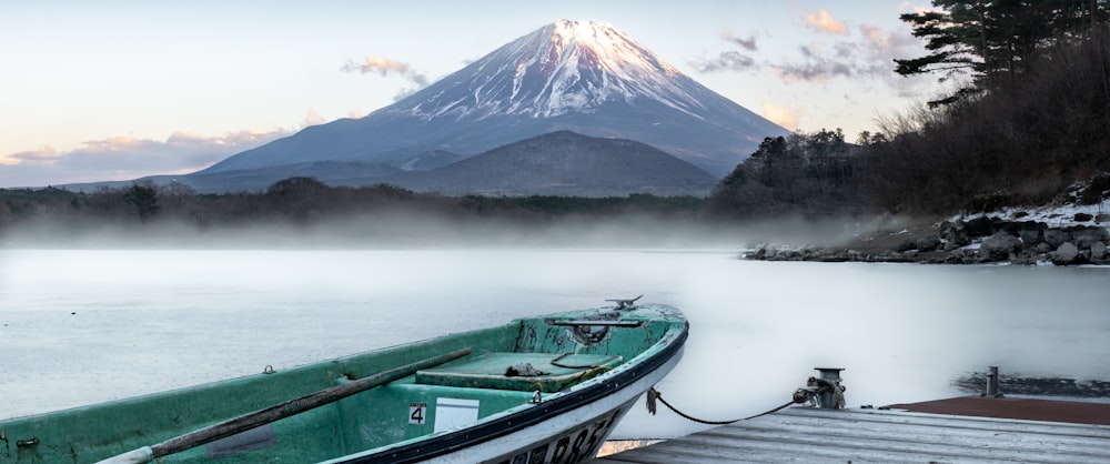 a green boat sitting on top of a lake next to a snow covered mountain