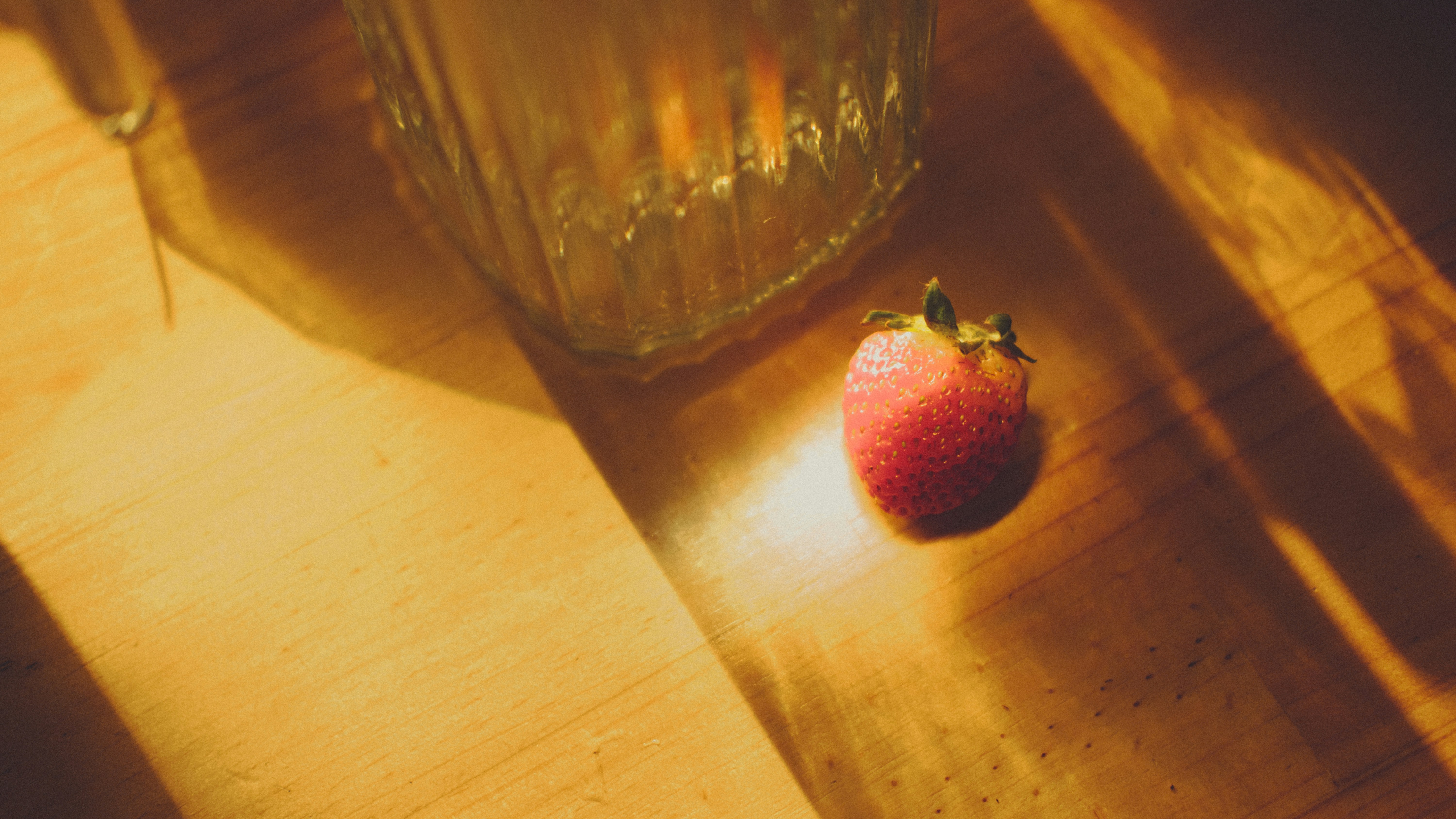 a strawberry sitting on a wooden table next to a glass